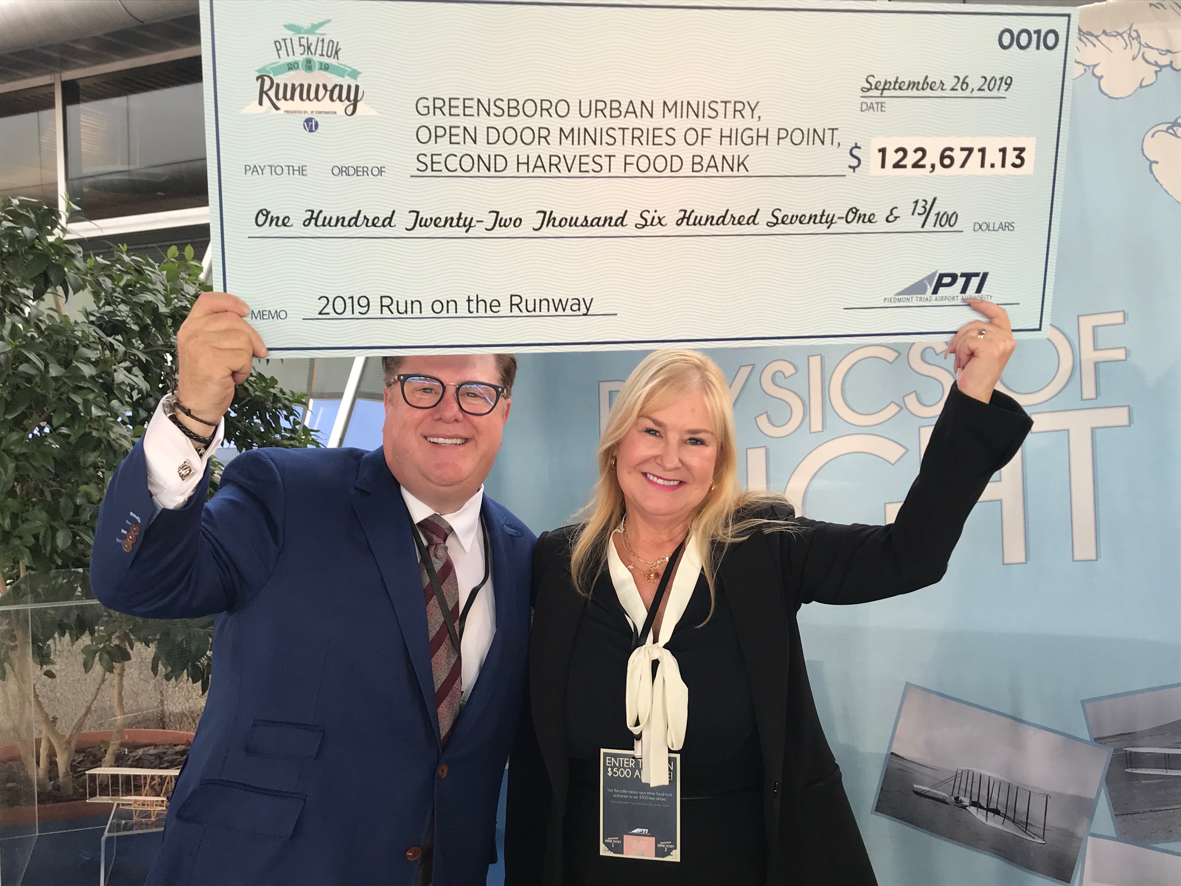 Paul and May Gayle Mengert holding check of funds raised for the PTI: 2019 Run on the Runway event to fight hunger in the Triad.