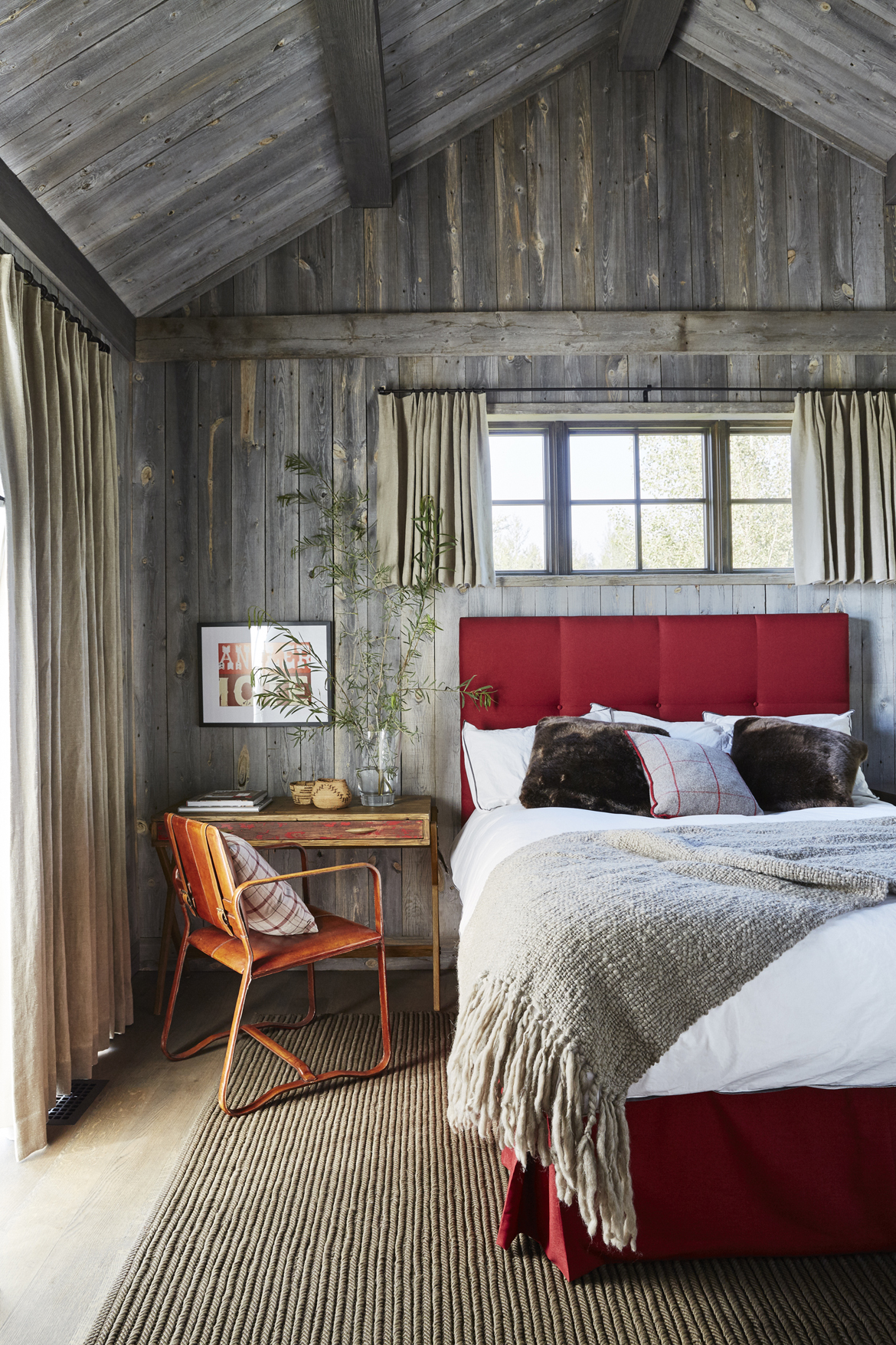 A surprising scarlet tufted headboard and bed skirt add a bold stroke of drama to patinaed wood walls in one of the guest cottage bedrooms by WRJ Design (photo by William Abranowicz).