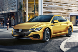 2020 Volkswagen Arteon yellow driving around city corner with people in background