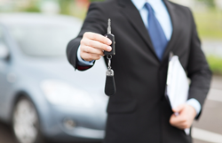 Salesman holding keys with a vehicle in the background.