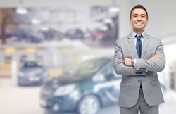 Car businessman standing in front of blurred out cars proudly