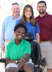 Two men and one woman stand behind a woman sitting in a wheelchair.