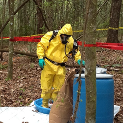 An emergency response technician investigates multiple abandoned drums discovered in the woods, a possible scenario under the contract
