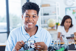 Independent African American male STEM student builds a robotic vehicle during robotics class. He is concentrating while he works on the project.