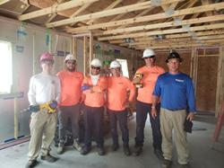 MaintenX team members stand in a building under construction wearing hardhats and holding power tools.