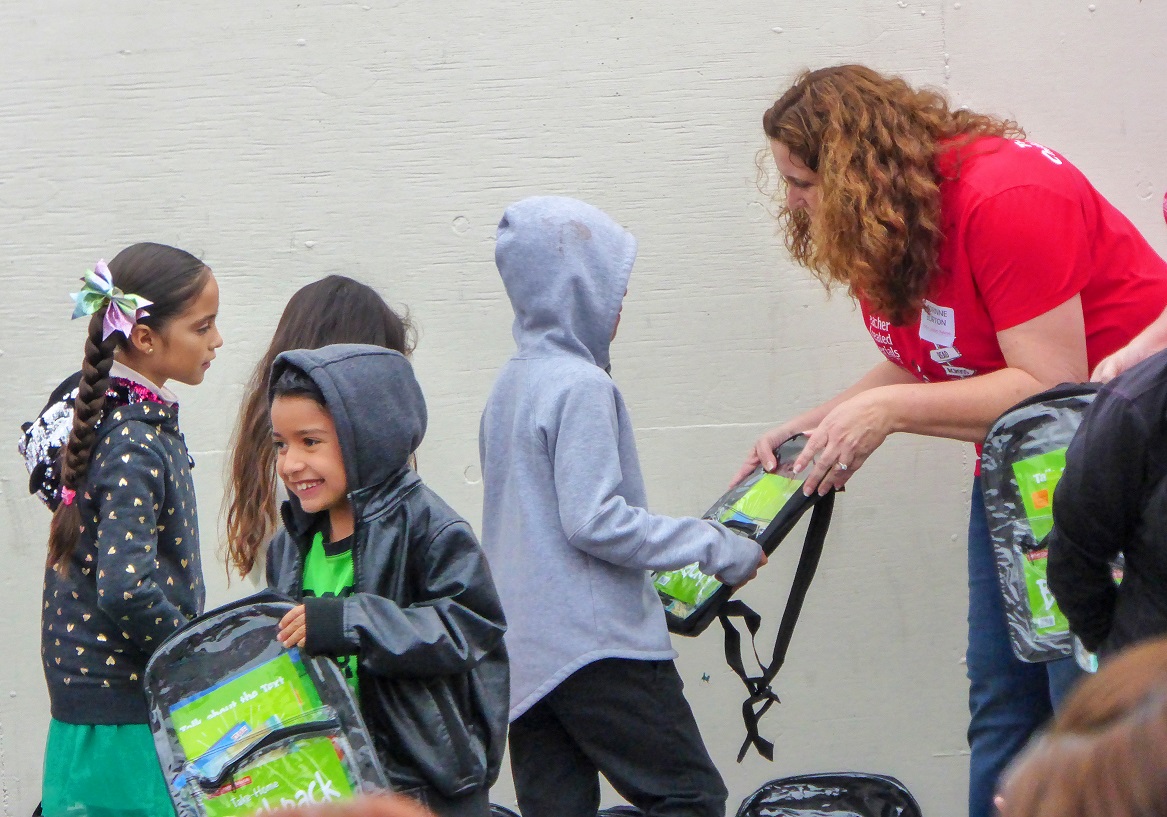 Corinne Burton, TCM President, hands out backpacks filled with reading and math activities