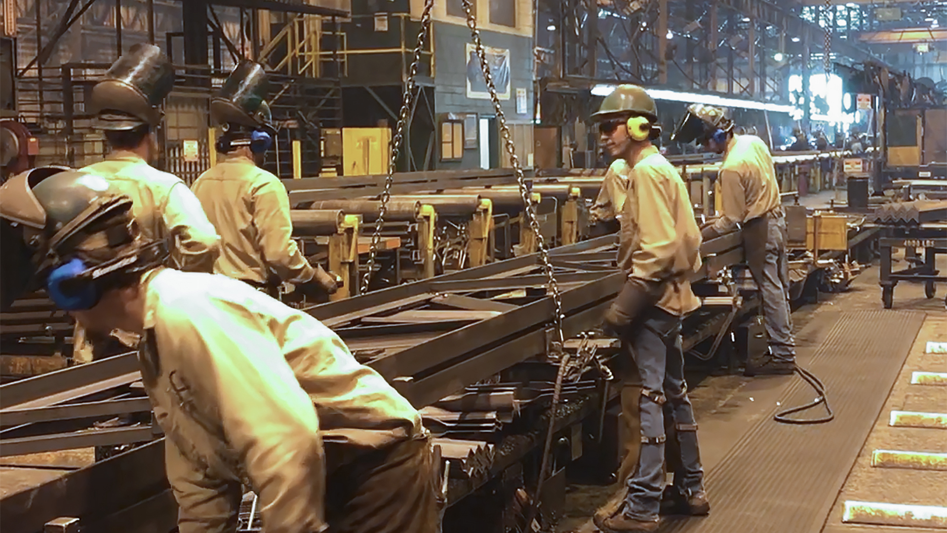 Steel fabrication workers use wireless headsets to communicate at social distances.
