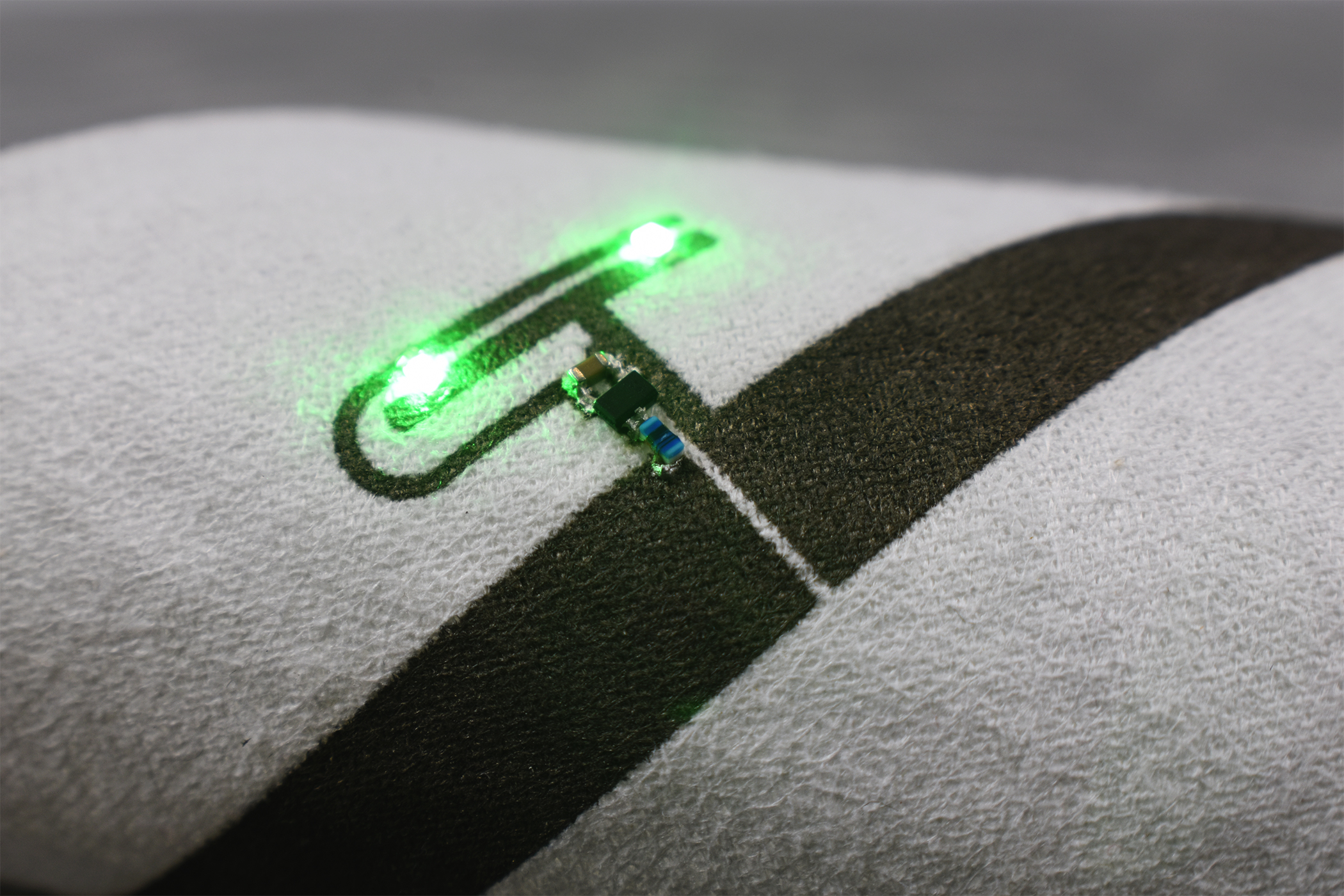 Liquid X’s particle-free inks can print circuitry on smart e-textiles that bend and flex without affecting functionality. LEDs mounted to printed traces light up via Powercast's wireless power tech.