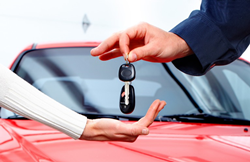 a car delivery salesman handing over the car keys and key fob to a new vehicle owner