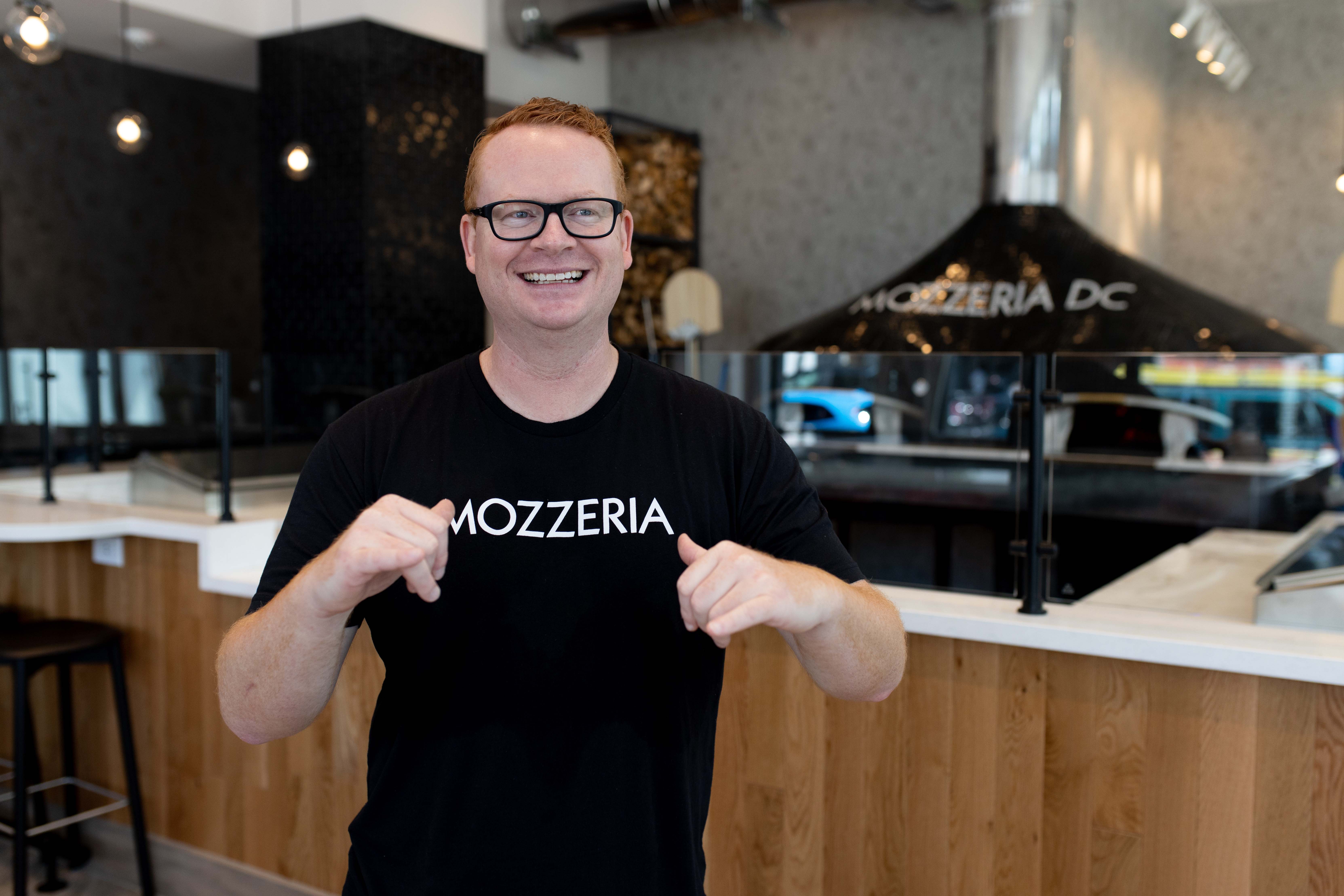 CEO Ryan Maliszewski displays Mozzeria's sign name, inspired by Italian Sign Language for "pizza"