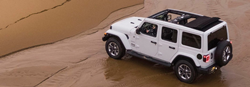 Rear driver angle of a white 2020 Jeep Wrangler parked on sand