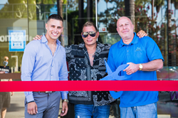 Ribbon cutting ceremony with a red ribbon across the bottom of the picture, about one third of the way up. Three men pose behind the ribbon, all smiling. From left to right is Nick Morgan, the Director of Business Development, Scott Storch, founding partner, and Steve Lobel, founding partner. Steve Lobel is holding a pair of blue scissors, motioning towards the red ribbon. Behind the men is the all glass entrance to the new alcohol and drug rehabilitation center, The Heavenly Center.