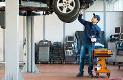 a mechanic at work in a garage in a jumpsuit working on a lifted car