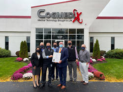 A group of people in facemasks standing outside the front entrance of Cogmedix accepting an award for FDA-compliant ventilators.