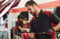A stock image of a male Toyota technician completing an oil change on a vehicle.