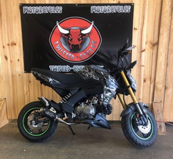 A black 2020 Kawasaki Z125 Pro parked in front of the Twisted Cycles dealership flag.