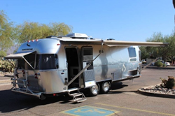 The front and side view of a 2019 Airstream International Serenity 27FB with its awnings out.