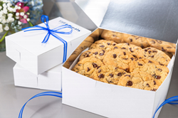 An open box of chocolate chip cookies sits next to two smaller boxes of cookies inside Tiff's Treats' signature blue and white packaging.