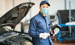 A mechanic by vehicle wearing a mask.