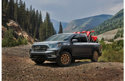 2021 Honda Ridgeline exterior shot with HPD package parked on dirt in a forest mountain clearing with motorbikes in its bed