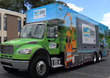 A truck that is a mobile unit for NC Works stands in front of a building. The sky is bright blue behind it. It has a design that incorporates illustrations of construction workers at work.