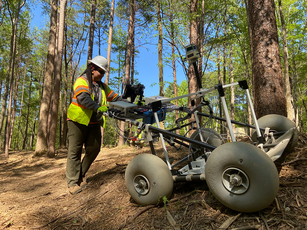 Technician scanning for UXO on steep terrain in wooded GPS-denied area.