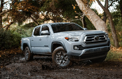 The front and side view of a light gray 2021 Toyota Tacoma driving in mud.