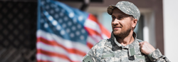 military man smiling walking out of building with American flag in background