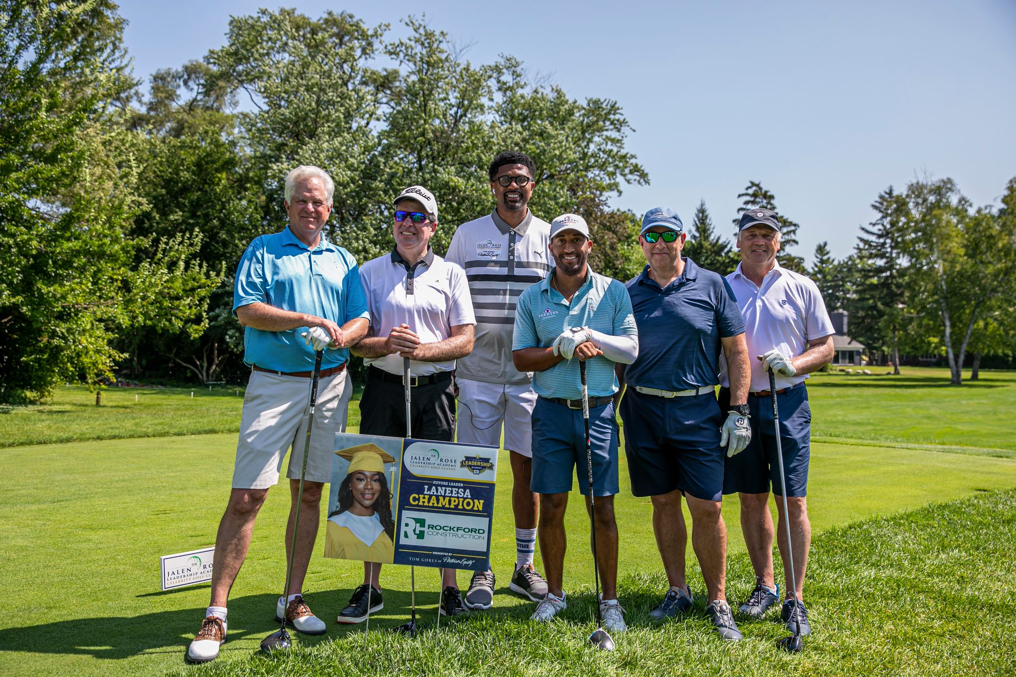 Team Platinum Equity alongside Jalen Rose and Willie Mack 3 pose with a JRLA graduate sign presented by Rockford Construction for the Jalen Rose Golf Classic, A PGD Global Production.