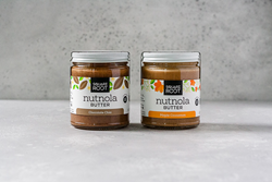 Two glass jars of new nut butters from Square Root Life. The left jar is the Nutnola Chocolate Chia flavor with a white and brown label. The right jar is the Nutnola Maple Cinnamon flavor with a white and orange label.