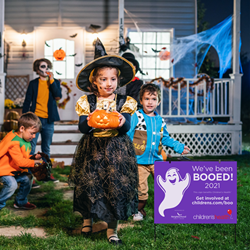 Kids dressed up in halloween costumes standing by a boo yard sign.