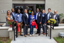 A diverse group of adults cut a ribbon in front of SOME's latest affordable housing building.