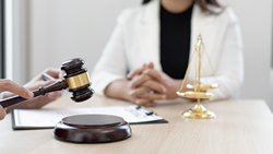 Medical liability concept: A nurse sits at a table with a clipboard, gavel, and golden scales of justice.