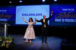 Leticia “Leti” Contreras and Thomas M. Mengler raise their arms in celebration on stage in front of a slide showcasing the number $165,000,000.