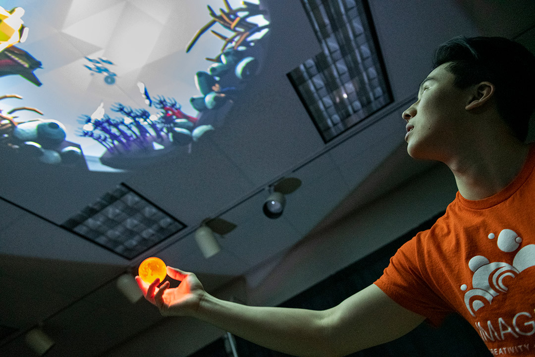 Student holding a ball that's projecting an ocean scene onto the ceiling. Credit: Elizabeth Lamark
