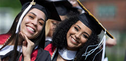 Two smiling female Hispanic/Latinx students wear caps and gowns at graduation.
