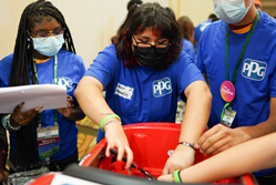 A Boys & Girls Clubs of America teen leader reviews the manual while a peer mentor demonstrates how to rewire the electric car that will be given to a toddler with mobility challenges.