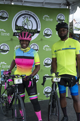 A Black man and woman in colorful  cycling gear stand with their bicycles in front of a banner that has the Lime Connect and Lime Ride logos on a green background.