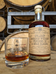 Image of a glass with the whiskey label etched holding whiskey and a bottle of the Tejas Collaboration with Ranger Creek. Bourbon finished in a mead barrel sitting on a barrel. 
