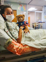 patient with stuffed animal in hospital bed.