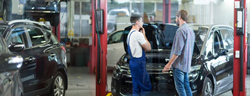 a technician and a man standing in front of an open hooded car in a service center