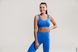 Young smiling fitness woman wearing sportswear standing over white wall background