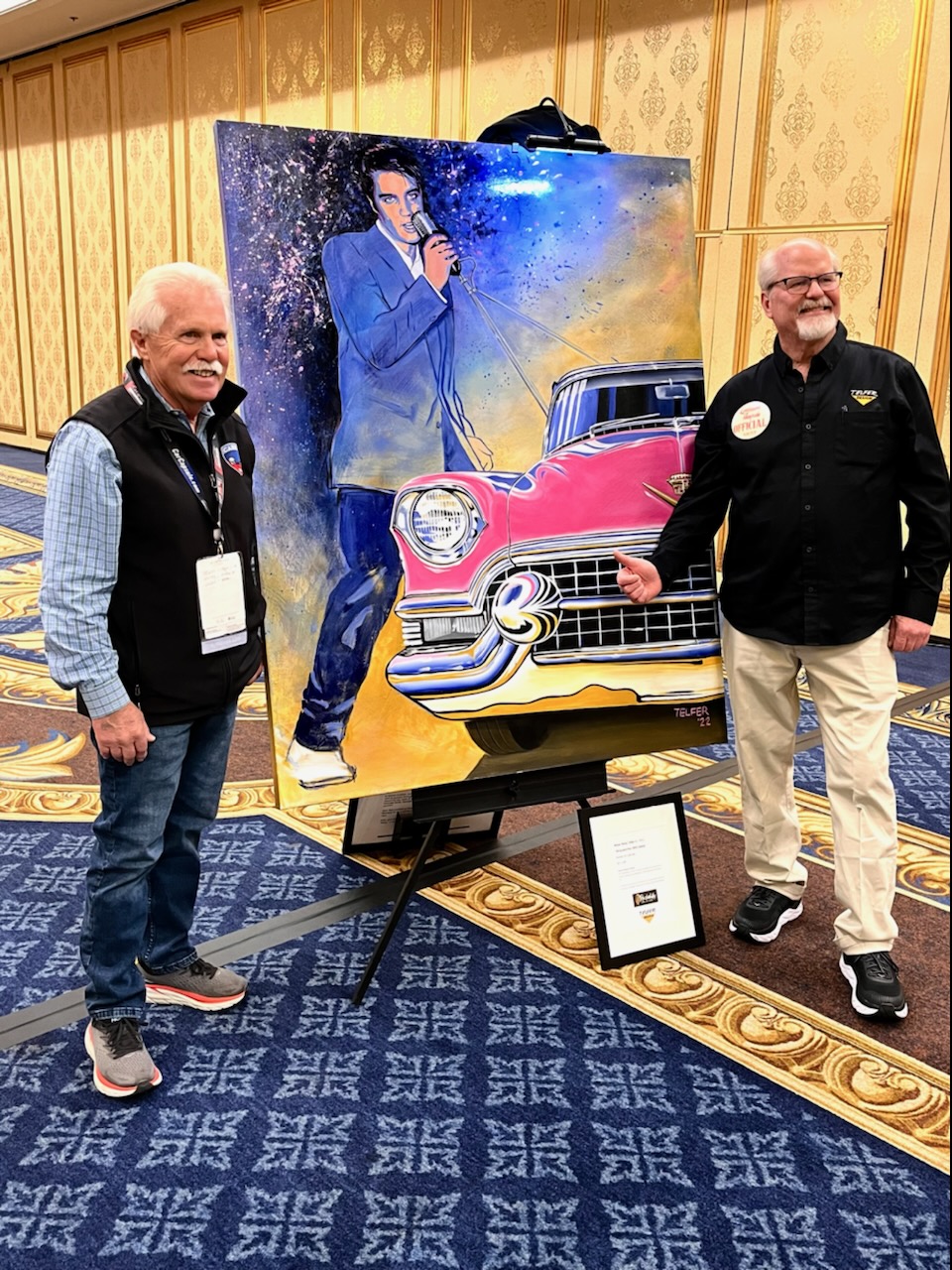 Wayne Carini from Chasing Classic Cars and artist Kelly Telfer pose next to the original “Elvis and His Cars” painting at the press conference during SEMA 2022