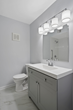 a newly renovated small bathroom showing mirror, vanity sink top, toilet, and lighting