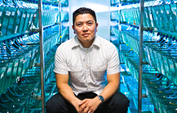 Duc Dong, Ph.D., an Asian American man in his 30s, seated in a vivarium full of green-blue fish tanks