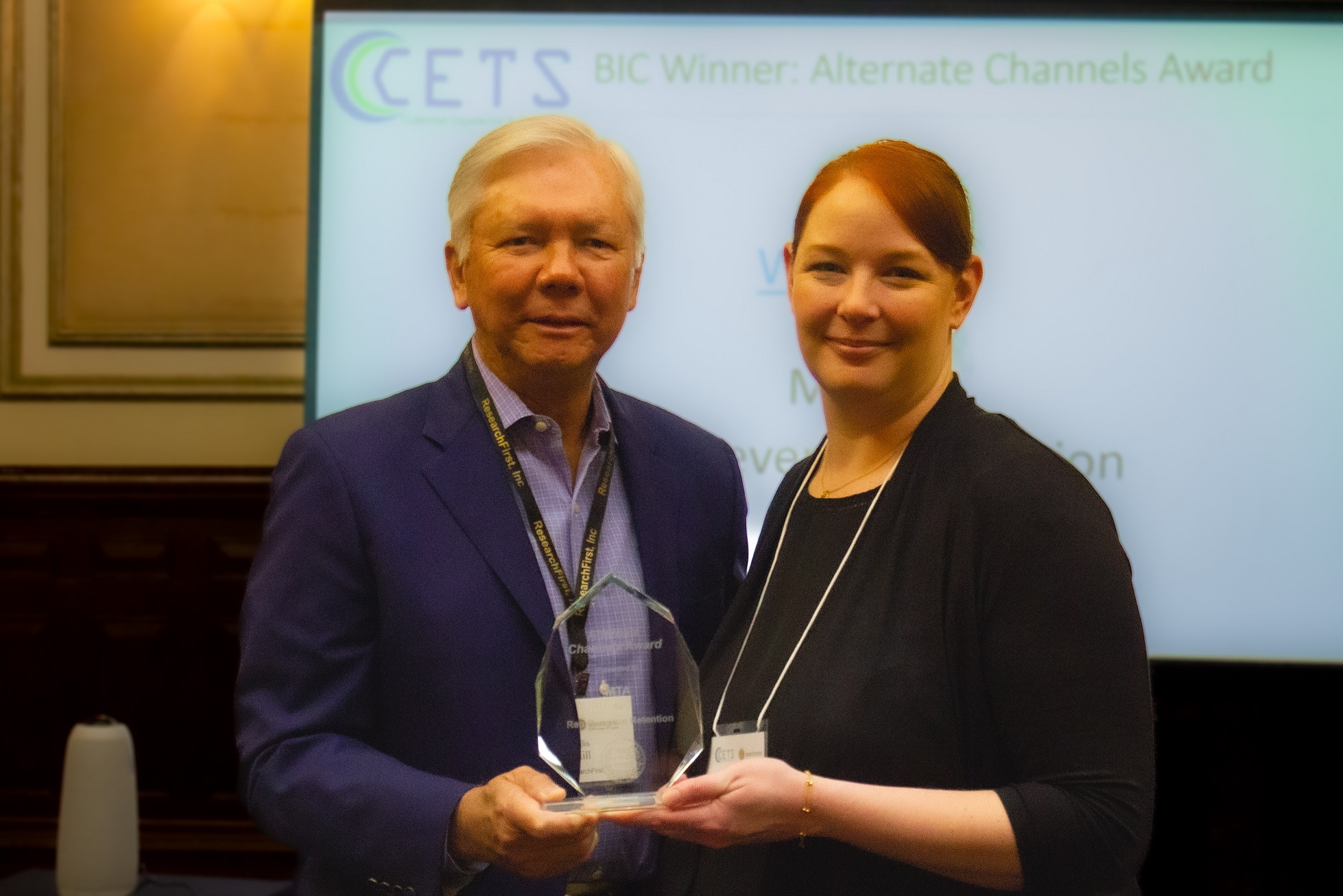 Jenna Deason, Sales Trainer at MTA (right) accepts the Alternate Channels Award from Ellis Hill, President of ResearchFirst (left).