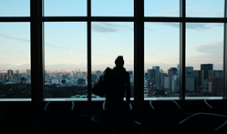 A business traveler stands in front of a window looking out on a city skyline